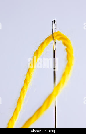 Un ago di cucitura con un filo giallo attraverso l'occhiello ,lungo attrezzo con un foro ad una sua estremità ,sfondo bianco , studio shot , composizione verticale ,m Foto Stock