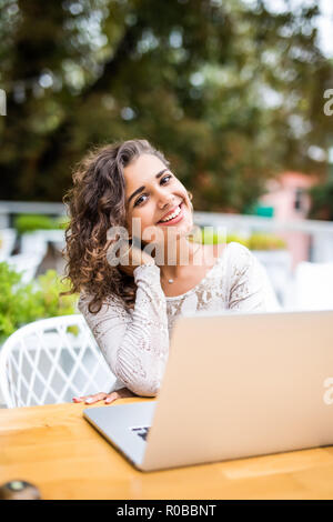 Bella giovane ricci donna latina con un'acconciatura afro lavorando al suo computer portatile in un coffee shop Foto Stock