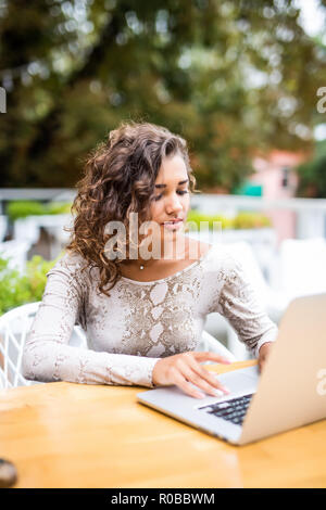 Bella giovane ricci donna latina con un'acconciatura afro lavorando al suo computer portatile in un coffee shop Foto Stock