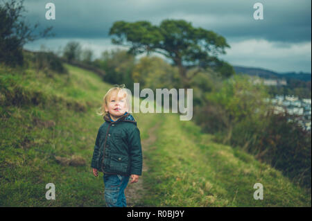 Un piccolo bimbo sta camminando sul pendio di una collina in autunno Foto Stock