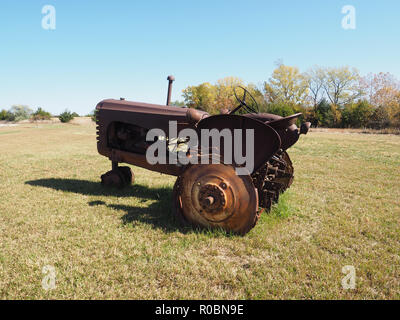 Un vecchio arrugginito trattore agricolo si trova in una zona di erba. Foto Stock