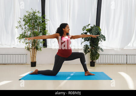 Giovane donna incinta a praticare yoga a casa Foto Stock