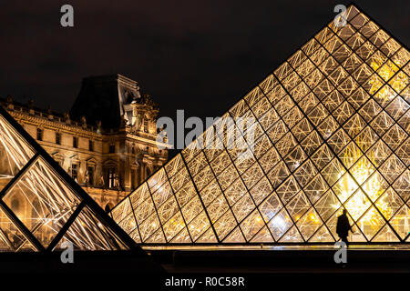 Parigi, Francia - 30 Settembre 2018: la brillante luce piramidi di vetro con silhouette di persone a piedi del museo del Louvre di notte. Foto Stock