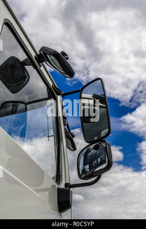 Il Cumulus bianche nuvole nel cielo blu sono riflesse nel lato windows e degli specchietti retrovisori di un carrello di grandi dimensioni. Foto Stock