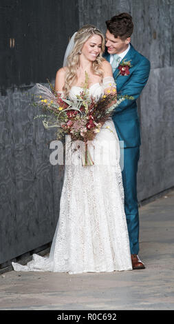 Gli sposi sorridenti e in posa di un abbraccio amoroso. La bella sposa è in possesso di un autunno bouquet e indossando un pizzo bianco abito da sposa Foto Stock