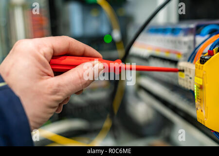 Primo piano di una mano con un cacciavite le opere in un armadio di controllo Foto Stock