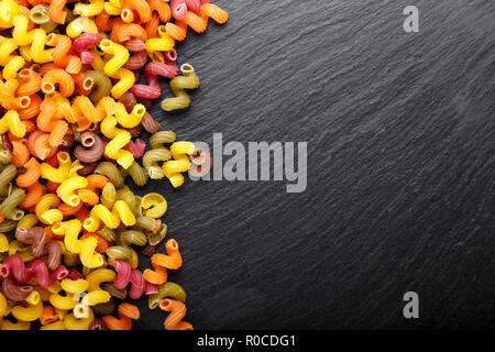 Spirale multicolore pasta sparsi su un nero ardesia sfondo. spazio per il testo Foto Stock