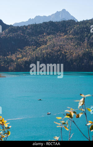 Vista sul lago color turchese "Alpsee" con pedalò su di esso in una calda giornata di sole in autunno. Hohenschwangau, Füssen, Baviera, Germania Foto Stock