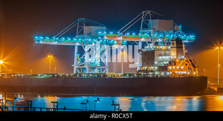 Nave nautico su una banchina durante il crepuscolo è scaricato con enormi gru moderne sotto illuminazione colorata Foto Stock