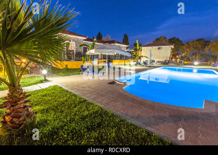 Esposizione lunga inquadratura di un resort per vacanze con mattoni di pietra e chalets acqua blu piscina su una calda notte Foto Stock
