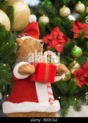 Un giocattolo portano vestiti da Babbo Natale in piedi contro un albero di Natale in possesso di una confezione regalo. Natale e Anno Nuovo concetto. Foto Stock