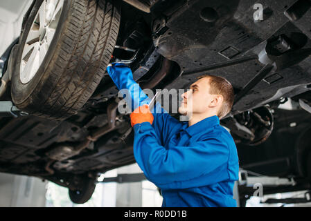 Meccanico con controllo di lampada auto i tubi flessibili del freno, stazione di riparazione. Servizio pneumatici, la manutenzione del veicolo Foto Stock