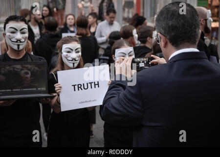 Un uomo visto scattare una foto dei partecipanti durante la protesta. Anonimo è un vegano gruppo di attivisti che indossa abiti neri mantenendo i laptop e cartelloni come essi dimostrano contro lo sfruttamento degli animali, il cubo della verità è una pacifica dimostrazione statica simile a una performance artistica. Foto Stock