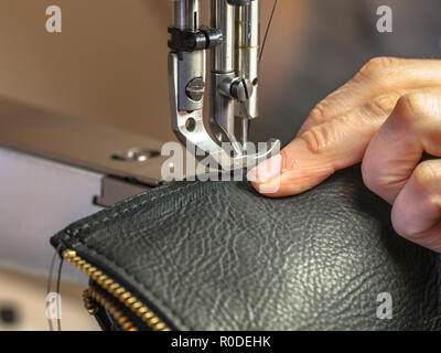 In pelle di macchina per cucire in azione in un workshop con le mani lavorando su una borsa a tracolla Foto Stock