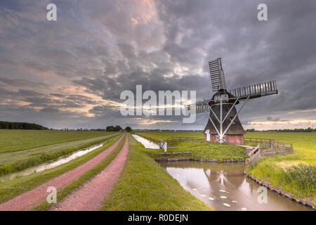 Vecchio mulino a vento di legno lungo una strada rurale nel paesaggio di polder nei Paesi Bassi. In passato questi edifici utilizzati per giocare un ruolo nella gestione delle acque Foto Stock