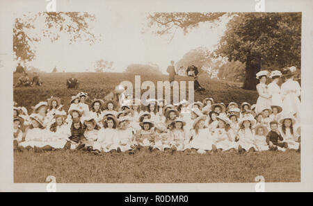Vintage Cartolina fotografica che mostra un gruppo di bambini della scuola Sat in un parco per un evento sconosciuto. Foto Stock