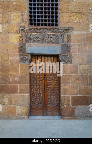 In legno porta ornati geometrici con motivi incisi su vecchi esterna decorata mattoni muro di pietra, il Cairo, Egitto Foto Stock