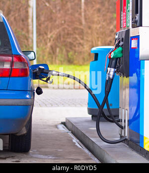 Auto blu alla stazione di gas essendo riempito con carburante contro prezzi gonfiati Foto Stock