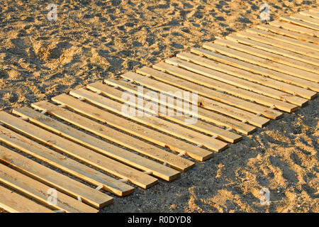 Lungo il tappetino in legno realizzato da nuove tavole parallele giacenti su di una spiaggia di sabbia Foto Stock