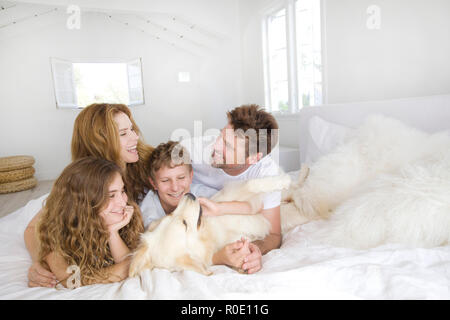 La famiglia felice la posa sul letto con cane Foto Stock