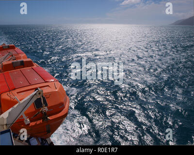 Una scialuppa di salvataggio su un lato di un traghetto al di sopra di un mare di un blu intenso Foto Stock