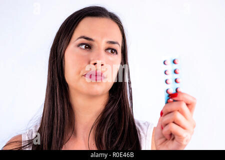 Pillole di rosso in blister in mano del giovane e bella donna che guarda a. Global industria farmaceutica per miliardi di dollari all'anno. Studio shot iso Foto Stock