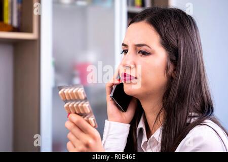 Pillole in blister in mano di preoccupato giovane donna chiamando al telefono al suo medico. Global industria farmaceutica per miliardi di dollari all'anno. Foto Stock