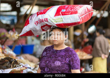 MANDALAY,MYANMAR,17 gennaio 2015: è una donna che porta un grande glutammato monosodico sacco sul suo capo in strada di Mandalay, Myanmar (Birmania). Foto Stock