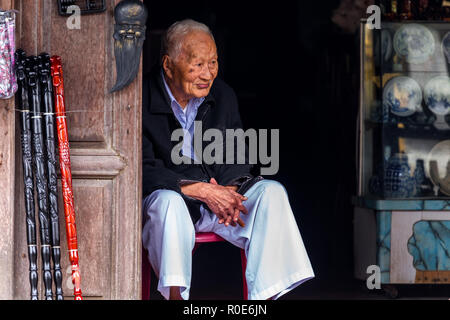 HOI AN, Vietnam, dicembre 14, 2014 : un venditore senior è seduto di fronte al suo artigianato souvenir shop nella città di Hoi An, Vietnam Foto Stock