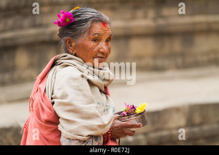 BHAKTAPUR, Nepal, Novembre 27, 2010: un senior donna che indossa abiti tradizionali sta portando alcune offerte per la mattina presto un tempio indù cerimonia Foto Stock