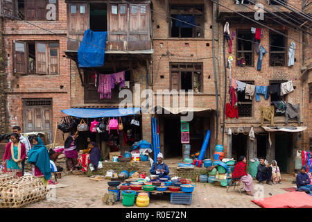 BHAKTAPUR, Nepal, Novembre 25, 2010: vista su un piccolo mercato con vestiti e cibo i venditori nella parte anteriore di un tradizionale edificio antico in Bhaktapur Foto Stock