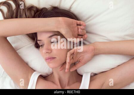 Giovane donna giaceva a letto con la mano sulla testa. Foto Stock