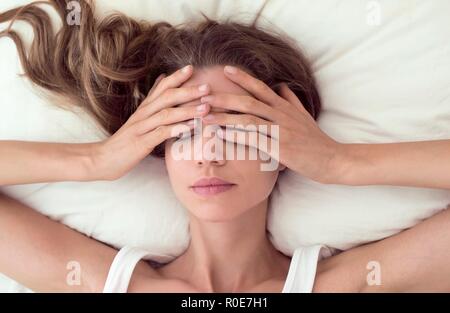 Giovane donna giaceva a letto e che coprono gli occhi. Foto Stock