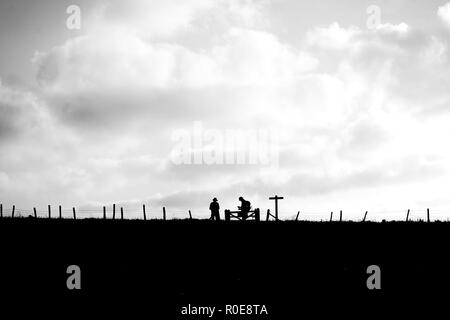In primo piano è un campo di distanza sono due escursionisti stagliano in piedi presso un cancello accanto a un segno posto con una staccionata in legno in tutta la Foto Stock