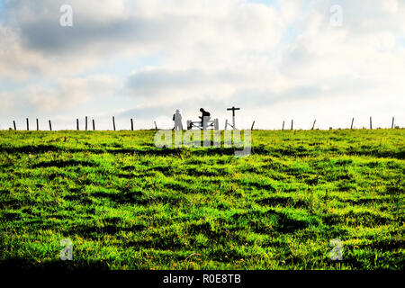Un campo verde in lontananza sono due escursionisti irriconoscibile stagliano in piedi presso un cancello accanto a un segno posto con una staccionata in legno in tutta la Foto Stock