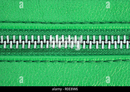 Zipper chiuso strettamente legare insieme i due strati di tessuto verde di prodotti tessili e in cuoio verde sotto un elevato ingrandimento vicino dettaglio fotografia come fashi Foto Stock