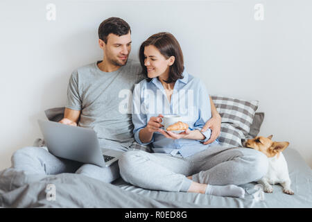 Affettuosa giovane in amore abbracciare in camera da letto, warch film on-line sul computer portatile, fare colazione e gustare atmopshere domestici e i loro preferiti pe Foto Stock