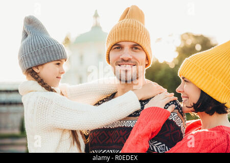 Graziosa piccola ragazza godetevi il tempo con i genitori, abbracciare il suo padre con grande amore, trascorrere il fine settimana in autunno insieme. Rilassata giovani in maglia cappelli ha Foto Stock