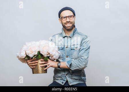 Felice felice maschio acquista un mazzo di fiori per la speciale occasione, indossa camicia di jeans e maglietta denim, isolato su sfondo bianco. Emotiona gioiosa Foto Stock