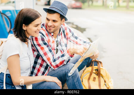 Ritratto di felice maschio e femmina, amici di viaggio, in appoggio su una panchina nel parco, cercando felicemente nella mappa, scegliendo il posto dove andare. Giovani turisti ha Foto Stock