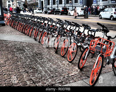 Lunga fila di biciclette con ruote di colore arancione in piazza della Scala a disposizione dei turisti. Milano, Italia Foto Stock