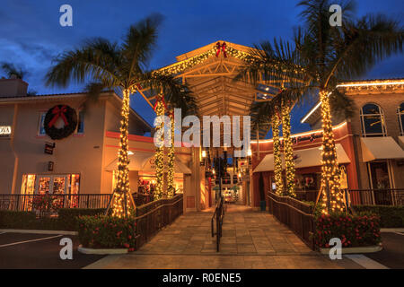 Naples, Florida, Stati Uniti d'America - 3 Novembre 2018: le luci di Natale incandescenza al tramonto del colorati negozi del villaggio su Venetian Bay in Naples, Florida. Pronto soccorso Foto Stock