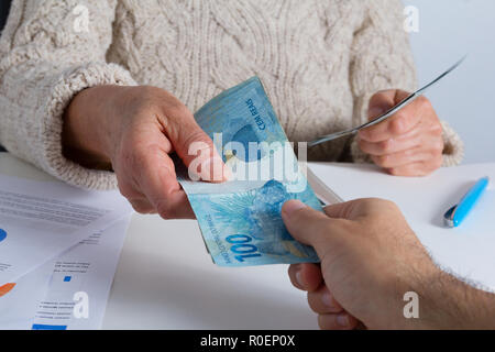 Valuta brasiliana, il denaro dal Brasile. Senior persona facendo un prestito a un giovane maschio presso l'ufficio. Foto Stock