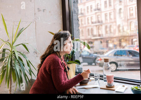 Donna che indossa un maglione di Nizza seduta vicino alla finestra nella caffetteria Foto Stock