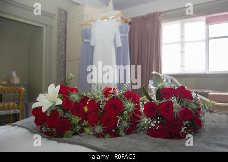 Bridal bouquet di rose rosse e abiti da sposa appesi in background su un spose il giorno del nostro matrimonio Foto Stock