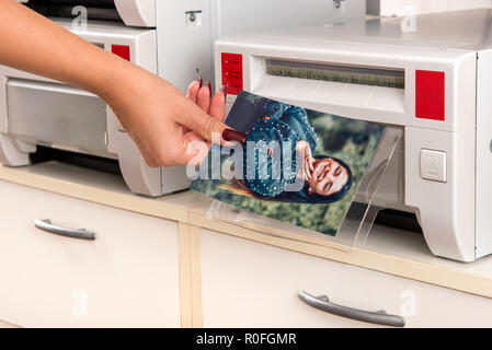 Donna assumendo un colore stampa fotografica di un sorridente bella donna da una stampante in una vista ravvicinata della sua mano e la macchina Foto Stock