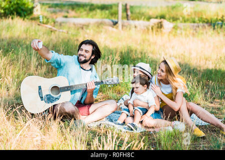 Padre tenendo selfie di famiglia con smartphone a picnic Foto Stock
