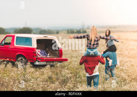 Giovani donne equitazione su fidanzati spalle in campo durante il viaggio in auto Foto Stock