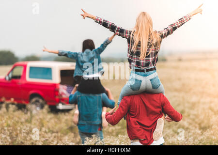 Vista posteriore di giovani donne equitazione su fidanzati alle spalle nel campo Foto Stock