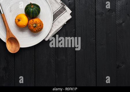 Autunno sfondo alimentare concetto. Vista dall'alto di zucche e cucchiaio di legno sul round piatto su tavoli in legno nero con copia spazio. Foto Stock